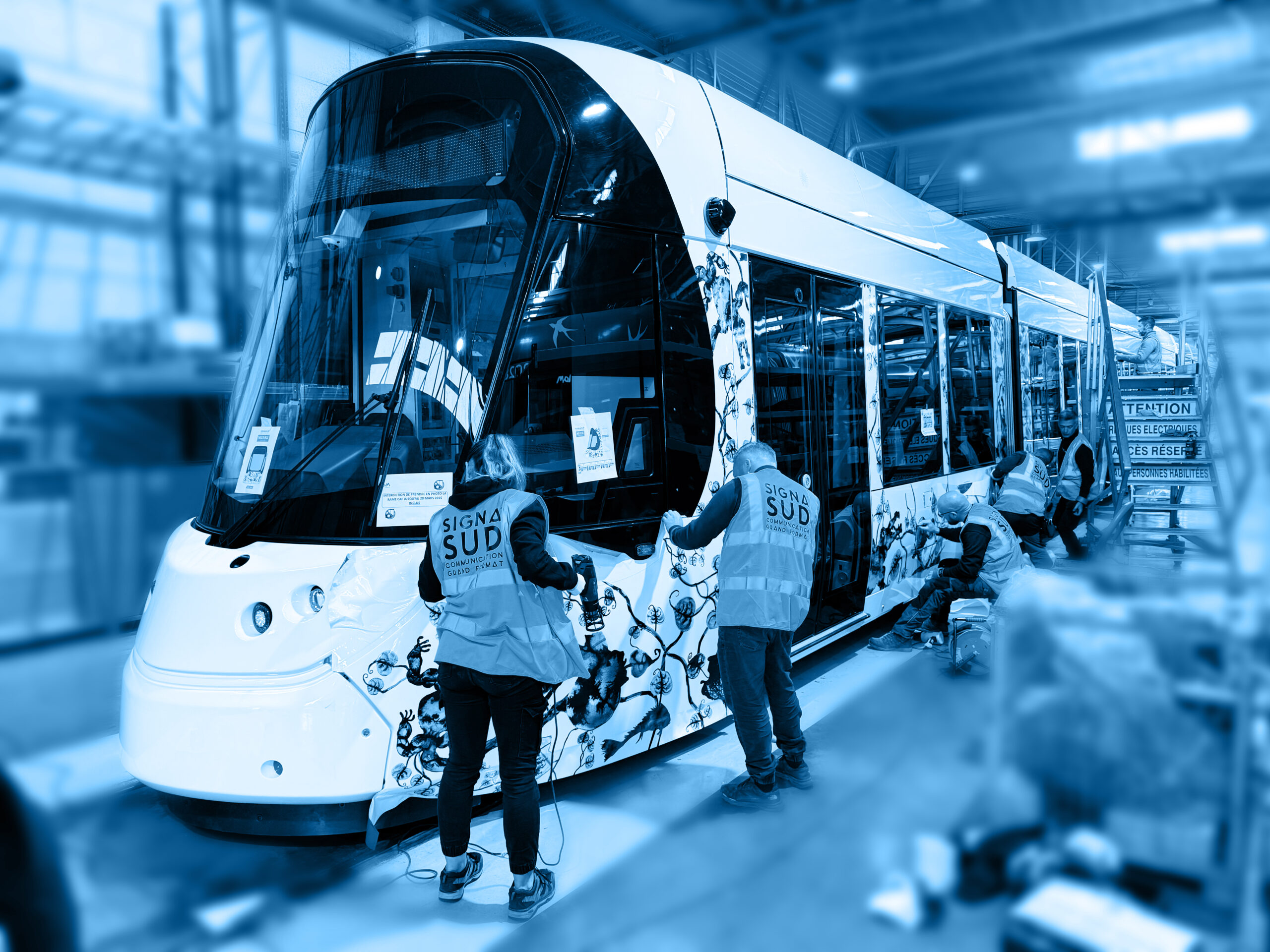 Habillage de tramway par SignaSud – Réseau transport Équipe de SignaSud posant un habillage adhésif sur un tramway en atelier