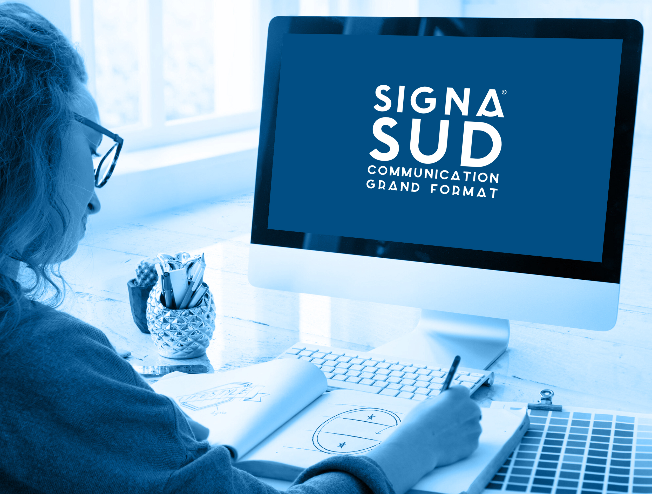 Studio graphique de SignaSud en pleine création visuelle Graphiste travaillant sur une maquette devant un écran affichant le logo SignaSud